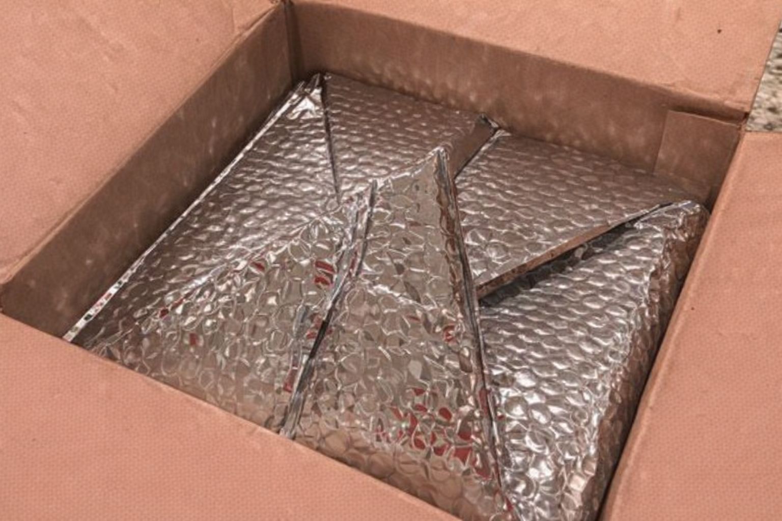 Geöffneter Versandkarton mit silberner Thermoisolierung für Lebensmittel.
